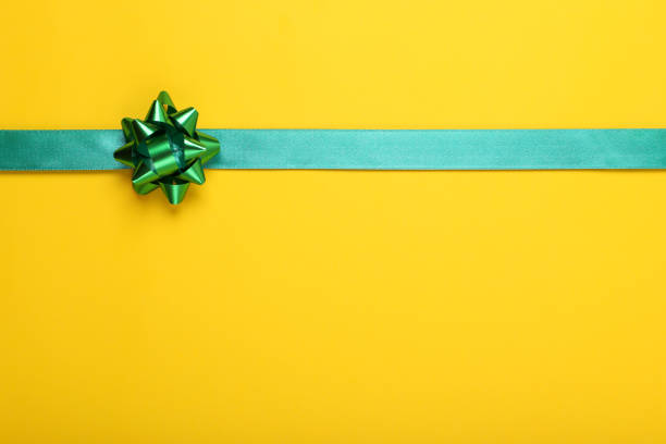 Green ribbon with bow on yellow background, top view. Space for text