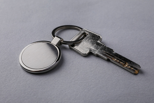 Key with metallic keychain on light grey background, closeup
