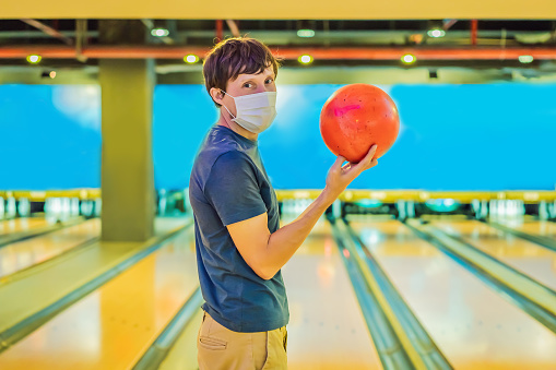 Mother and son plaing bowling and wearing a protective mask .