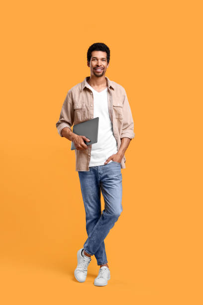 istock Happy man with laptop on orange background 1707069931
