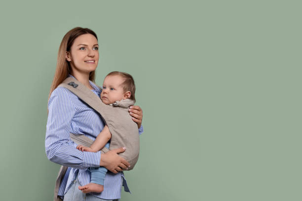 istock Mother holding her child in sling (baby carrier) on olive background. Space for text 1707074180