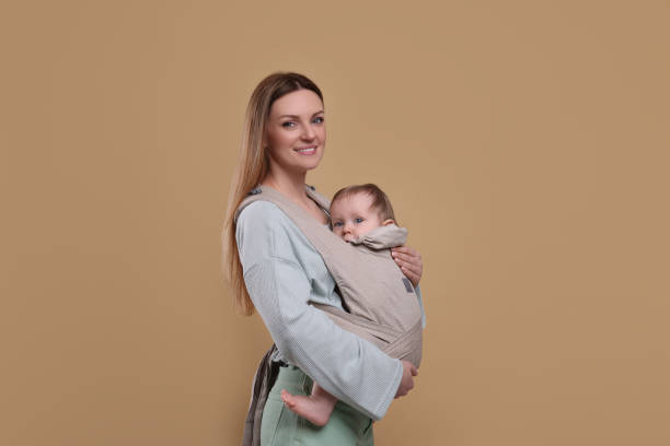 istock Mother holding her child in sling (baby carrier) on light brown background 1707074720