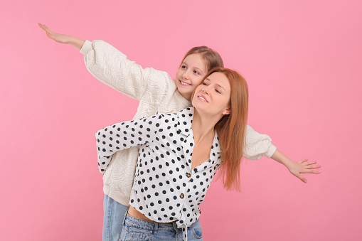 Happy mother with her cute daughter on pink background