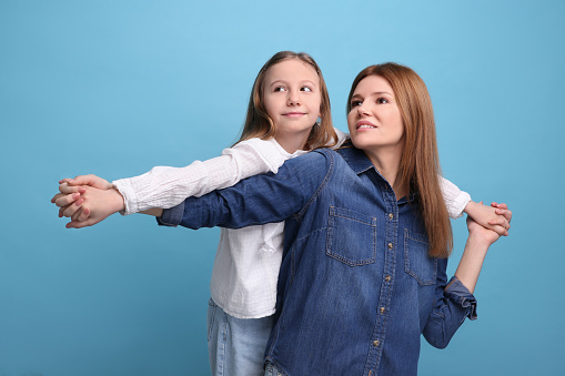 Portrait of happy mother and her cute daughter on light blue background