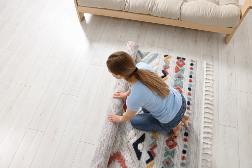 Woman unrolling carpet with beautiful pattern on floor in room, view from above. Space for text