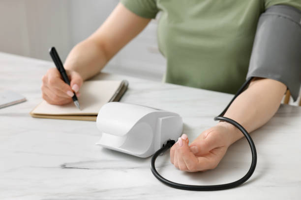 istock Woman measuring blood pressure and writing it down into notebook in kitchen, closeup 1707086564