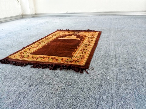 An orange prayer mat with a mosque building motif on a blue carpet