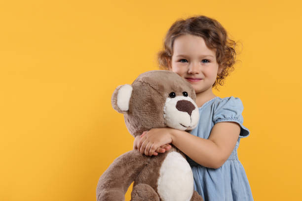 istock Cute little girl with teddy bear on orange background, space for text 1707088457