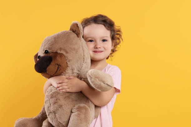 istock Cute little girl with teddy bear on orange background 1707089089