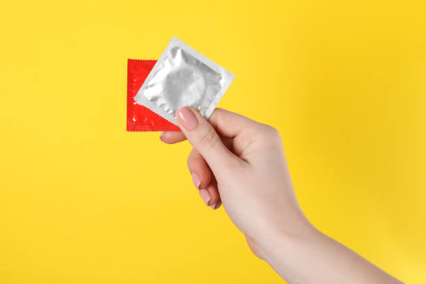 mujer sosteniendo condones sobre fondo amarillo, primer plano - condom sex sexually transmitted disease aids fotografías e imágenes de stock