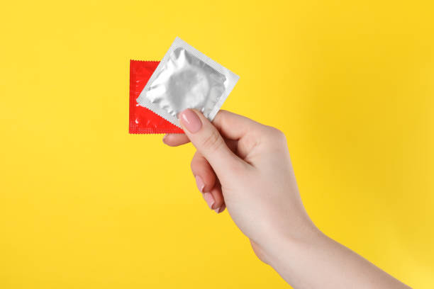 노란색 배경에 콘돔을 들고 있는 여자, 클로즈업 - condom sex sexually transmitted disease aids 뉴스 사진 이미지