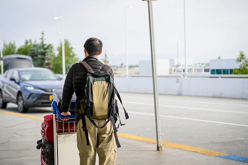 Man pushing the luggage trolley and walking towards a parked car outside the airport.