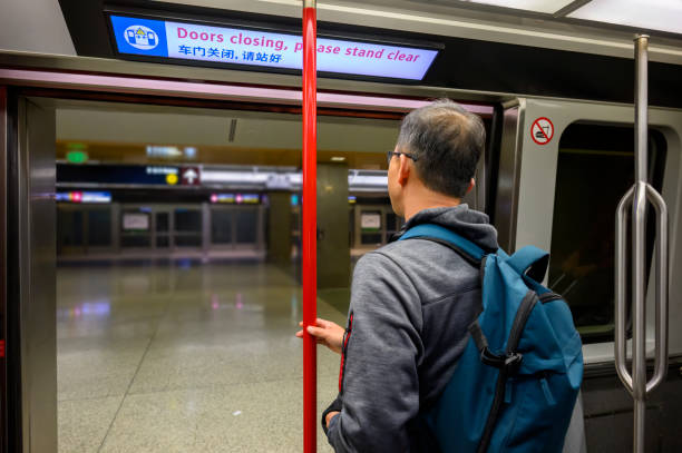 空港の鉄道リンクの開いたドアのそばに立っている男。英語と中国語のメッセージで頭上にネオンボード - ドアが閉まり、はっきりと立ってください。 - train door vehicle door open ストックフォトと画像