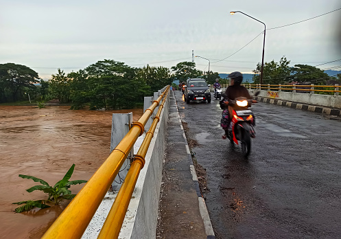 Sukoharjo, Indonesia November 19,2022 : Witness the resilience of a motorcyclist as they navigate a flooded bridge, rising above the surging waters. This photograph captures the determination and courage of those who forge ahead in the face of adversity, crossing turbulent rivers on their two-wheeled companions.