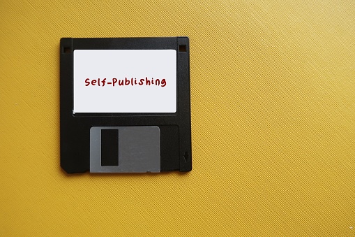 Floppy disk on yellow copy space with text SELF-PUBLISHING, act of writer publish piece of creative work book media independently at own expense, without the use of traditional publishing house