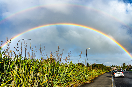 A complete arch of the rainbow with its second bow over the horizon appears on a rainy and sunny day in Mt Roskill
