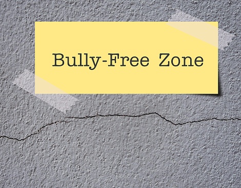 Grey rough cement cracked wall copy space background with text on note BULLY-FREE ZONE, anti bully policy - stop or reduce bullying, shame , abuse to create safe and welcoming space in social or school