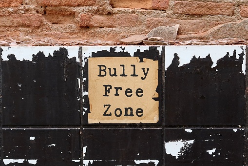 Old vintage ruined brick grunge cracked tiled wall background with text on paper BULLY FREE ZONE, anti bully policy , stop or reduce bullying, shame , abuse to create safe and welcoming space in social