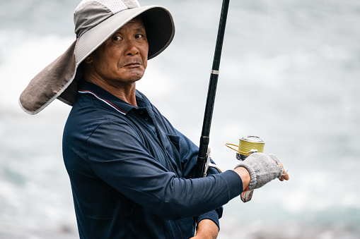 Amidst a peaceful fishing expedition, a middle-aged man adeptly holds a fishing rod, his experienced hands poised for the catch. This tranquil scene encapsulates the timeless connection between man and nature, where the pursuit of patience and skill merges with the serenity of the natural world.