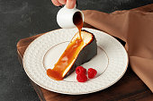 Piece of cheesecake with pouring caramel sauce on plate
