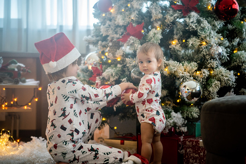 Boy and girl in pajamas decorating Christmas tree at home