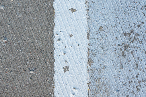 Close-up of the surface of an old concrete railway platform. There is a diamond-shaped corrugation and a white boundary stripe. Background.