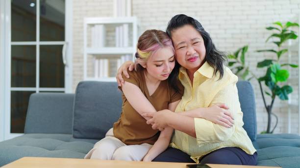istock Happy Asian parent mother with young daughter hugging cuddle together while sitting on sofa at home. Young Asian woman and eldery mother spending time together at home. Family day concept 1707442105