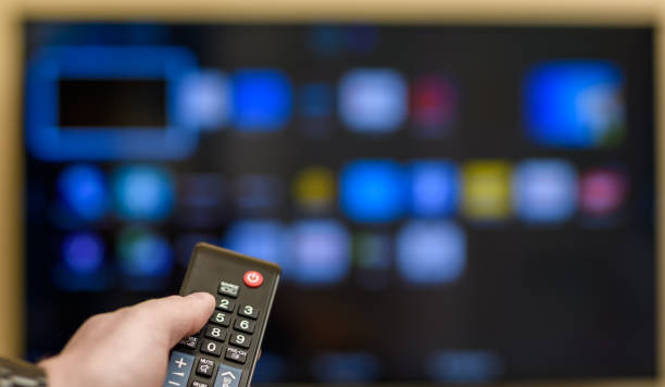 istock TV remote control held in hand, TV on in the background 1707465465
