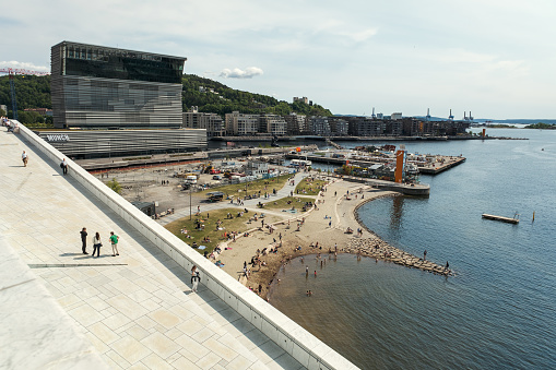 Oslo, Norway - June 3rd 2023: View from the Opera House of the city beach full of people on the weekend in front of the Munch museum in the newly developed Sørenga area with modern buildings