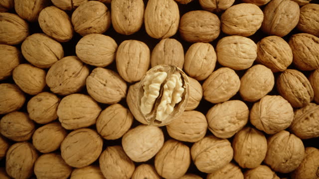 A top-down view of a partially peeled walnut slowly rotating and falling down among a pile of other nuts. Macro slide, in slow motion.