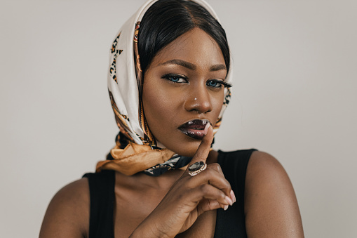 Portrait of a beautiful young black woman wearing an elegant black dress and headscarf, studio shot in front of a white background
