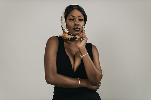 Portrait of a beautiful young black woman wearing an elegant black dress and headscarf, studio shot in front of a white background