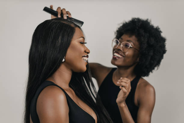 Young black woman having her hair styled for a photo shoot Beautiful young black woman a fashion model having her hair styled by a professional hair stylist for a photo shoot, a studio shot in front of a white background black hair stock pictures, royalty-free photos & images