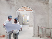 Couple holding blueprints in house under construction