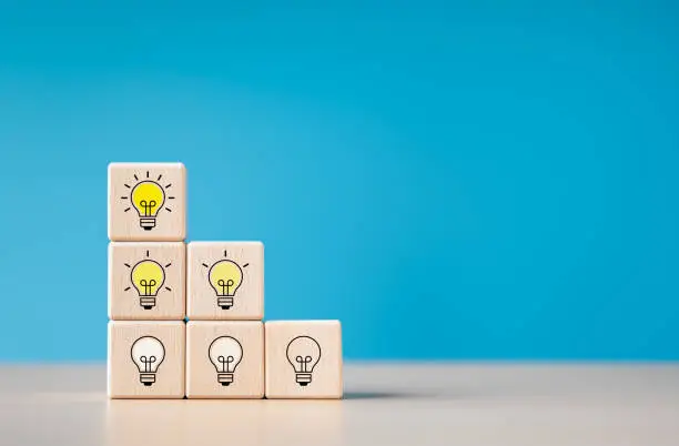 Photo of Innovation and creativity idea concept. Teamwork and brainstorming for business start-up creative ideas and solving problems. Wooden blocks with glowing light bulb icons with dim brightness levels.