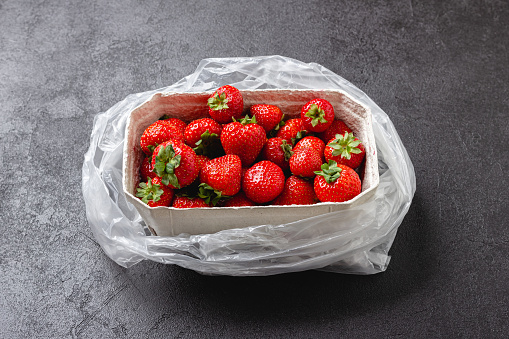 Fresh strawberries in paper basket. Sweet red berries on black table. Healthy and organic dessert.