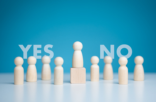 Volunteers, candidates, constituency electorates. Wooden figure dolls stand above podium among others with vote yes or no words. Referendum, Poll, Open-mindedness, Public hearing, Elections concept.