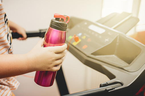 Young girl running on the treadmill with a sports water bottle in hand