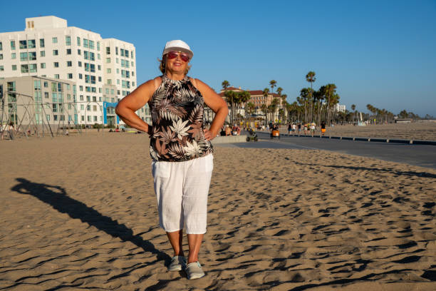 starsza kobieta w okularach przeciwsłonecznych ciesz się spacerem po plaży w los angeles - party beach indian ethnicity adult zdjęcia i obrazy z banku zdjęć