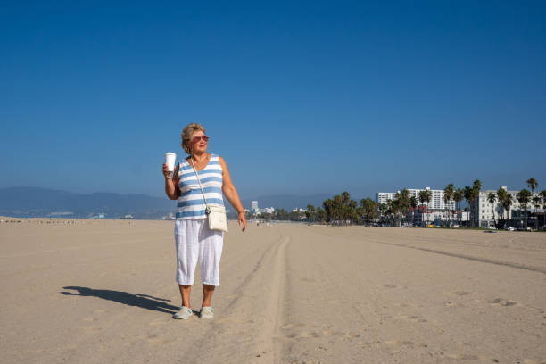 starsza kobieta w okularach przeciwsłonecznych ciesz się spacerem po plaży w los angeles - party beach indian ethnicity adult zdjęcia i obrazy z banku zdjęć