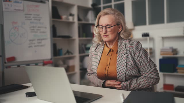 Woman office manager in her 50s feeling abdominal pain while working on laptop