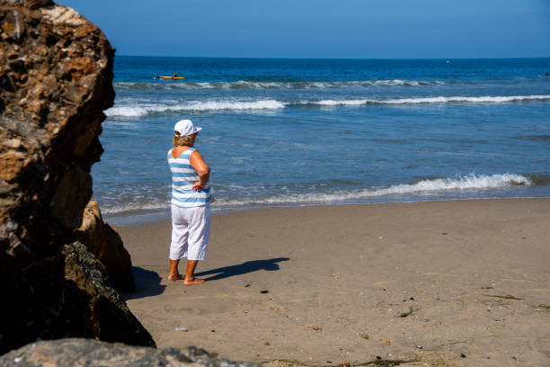 starsza kobieta w okularach przeciwsłonecznych ciesz się spacerem po plaży w los angeles - party beach indian ethnicity adult zdjęcia i obrazy z banku zdjęć