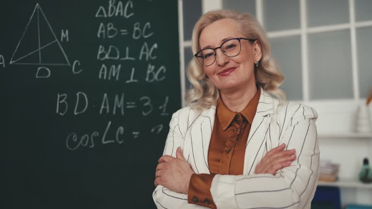 Portrait of smiling woman geometry teacher standing near chalkboard in class