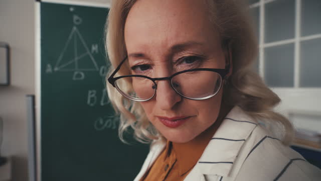 Funny strict mathematics teacher in her 50s looking at camera, geometry lesson
