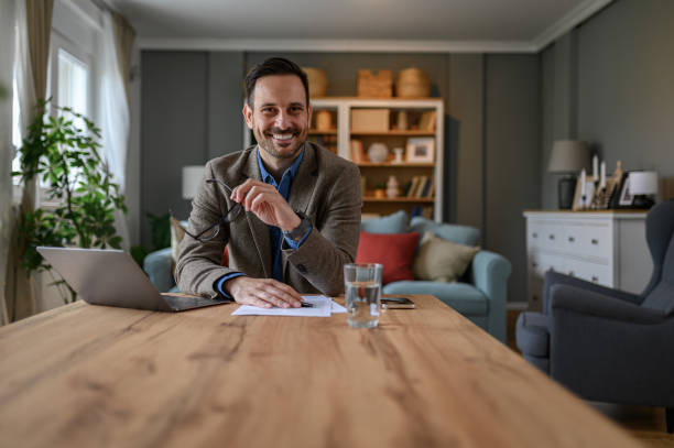istock Smiling male professional holding glasses and looking at camera while working over laptop at desk 1707648782