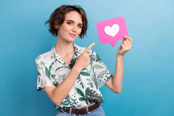 Photo of Photo of satisfied pretty girl with bob hairstyle dressed colorful blouse indicating at pink like icon isolated on blue color background