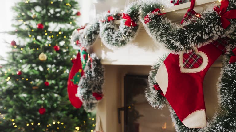 Empty Shot Depicting the Magic of Holidays on a Peaceful Snowy Christmas Morning: Close Up on Decorated Fireplace with Stockings Next to a Christmas Tree. Green and Red Garlands, Ribbons and Lights