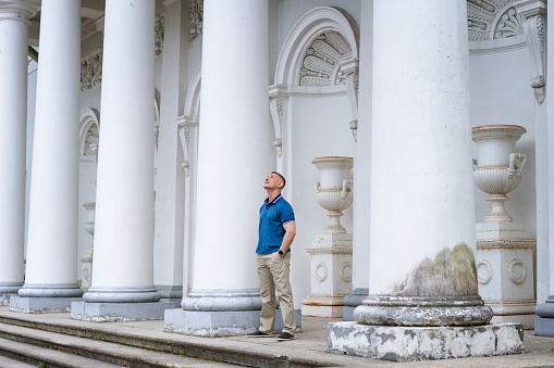 a man in casual clothes stands near the columns of a white building