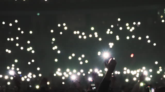 Many people waving phone flash light. Music concert atmosphere. Fans crowd enjoy