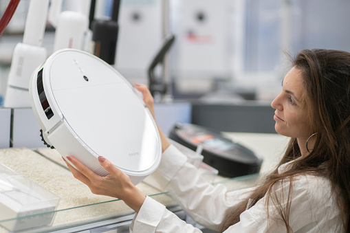 female person in the electronics store choosing the robot vacuum cleaner
